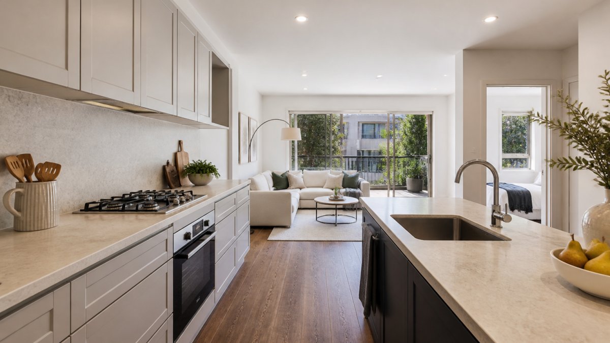 A freshly renovated apartment kitchen with stone benchtops, new cabinetry and a light-filled living area visible beyond, styled as a rental-ready investment property