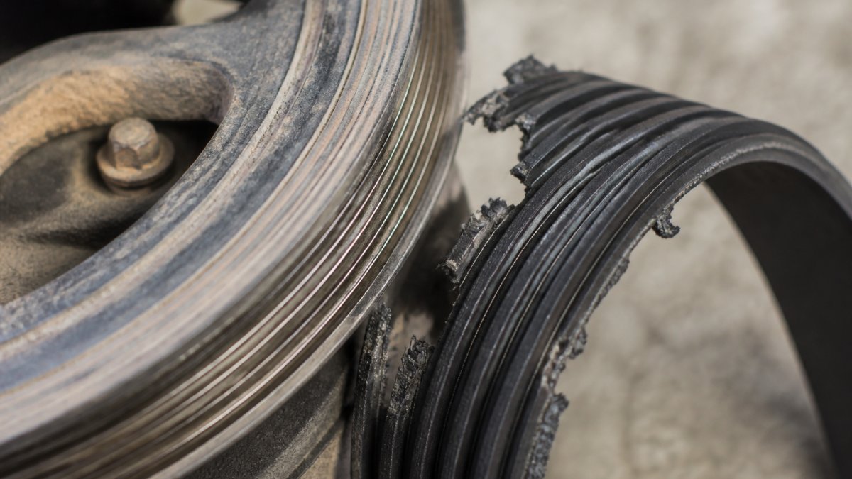 Close-up of worn pulley groove with visible scoring and friction damage alongside a shredded serpentine belt showing uneven wear patterns