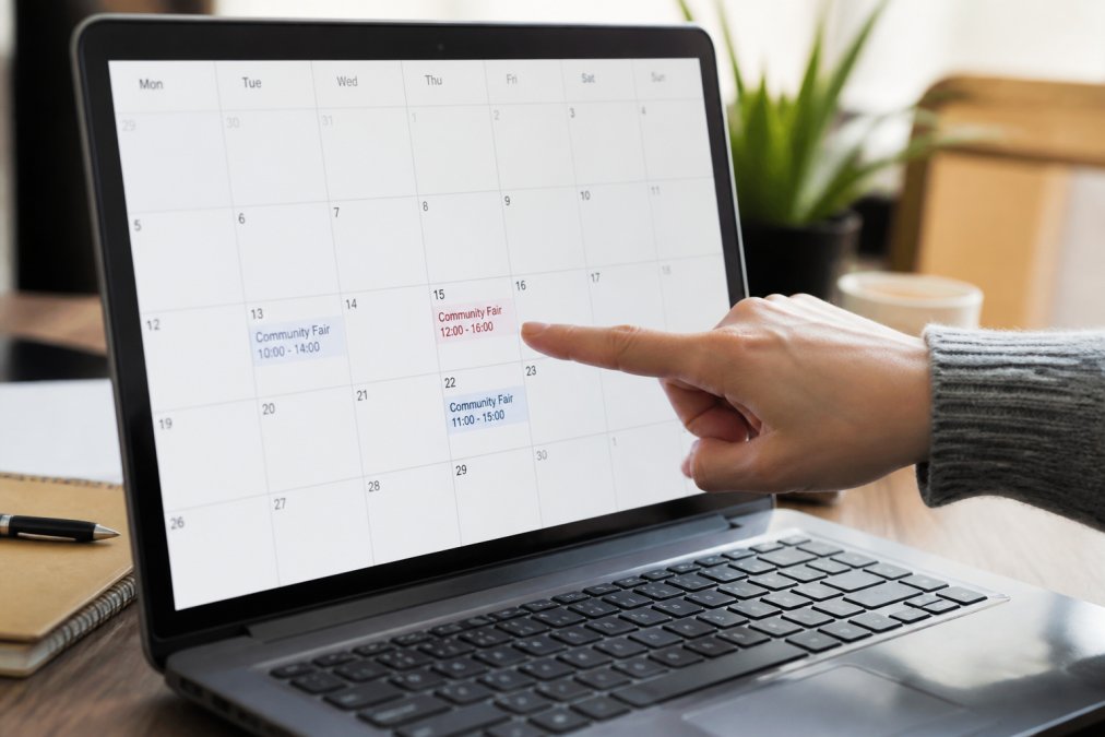Close-up of a laptop screen showing a calendar with conflicting event times highlighted, with a hand pointing to discrepancies
