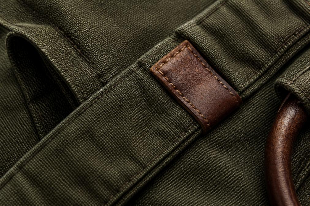 Close-up of premium fabric texture showing dense weave pattern with visible stitching detail and leather accent on luxury garment, natural studio lighting
