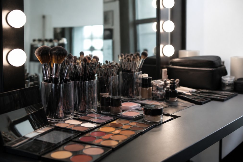 Professional makeup artist's workspace with premium brushes arranged in holder, colour palettes, cosmetics, and lighting setup on elegant vanity table