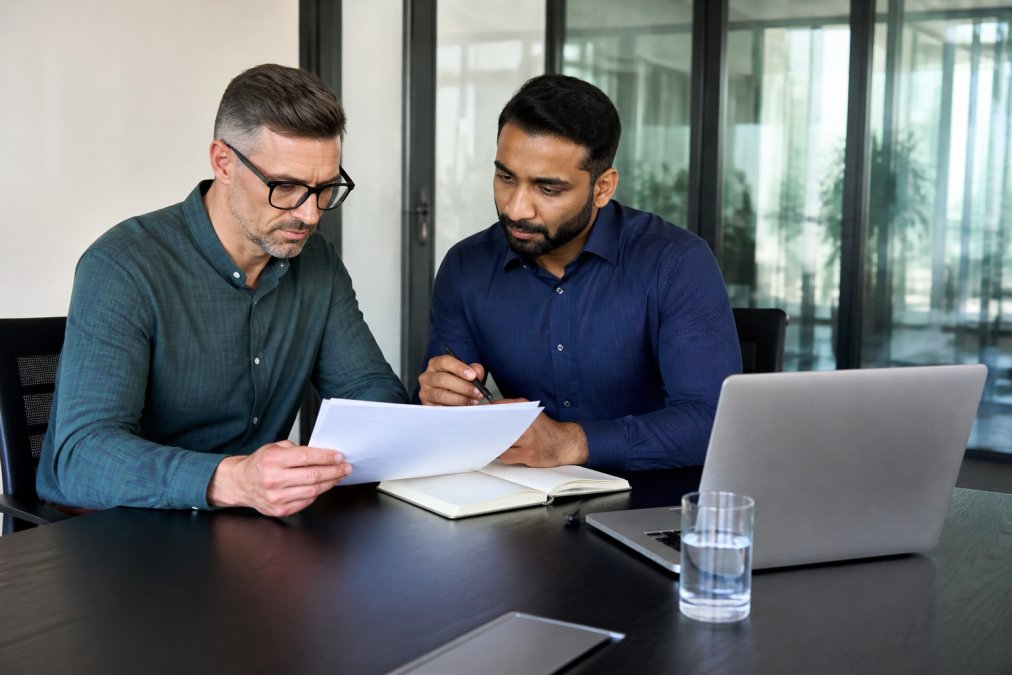 A small business owner and an IT consultant reviewing a financial report and a laptop with security dashboard on the screen in a modern office conference room