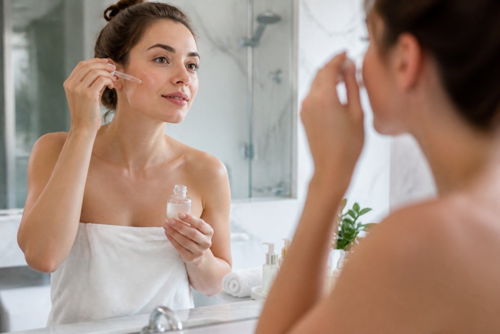 Woman with glowing skin applying hydrating serum after a microneedling safe treatment in a bright bathroom