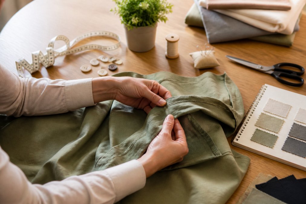 Close-up of hands carefully examining fabric seams, stitching details, and garment construction on a laid-out piece of clothing with natural lighting