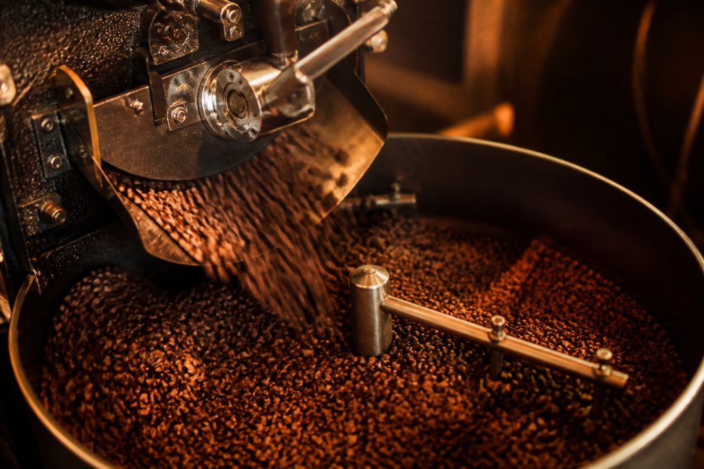 Close-up of fresh organic coffee beans being roasted in-house, with warm amber and orange light highlighting the beans' deep brown color and texture as they tumble in a roaster drum