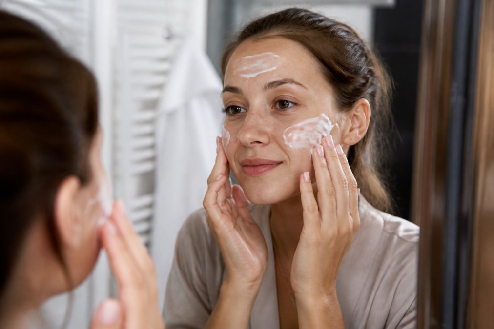 Close-up van handen die zonnebrandcrème SPF 30+ aanbrengen op gezicht na PDT-behandeling, beschermende ingrediënten zichtbaar