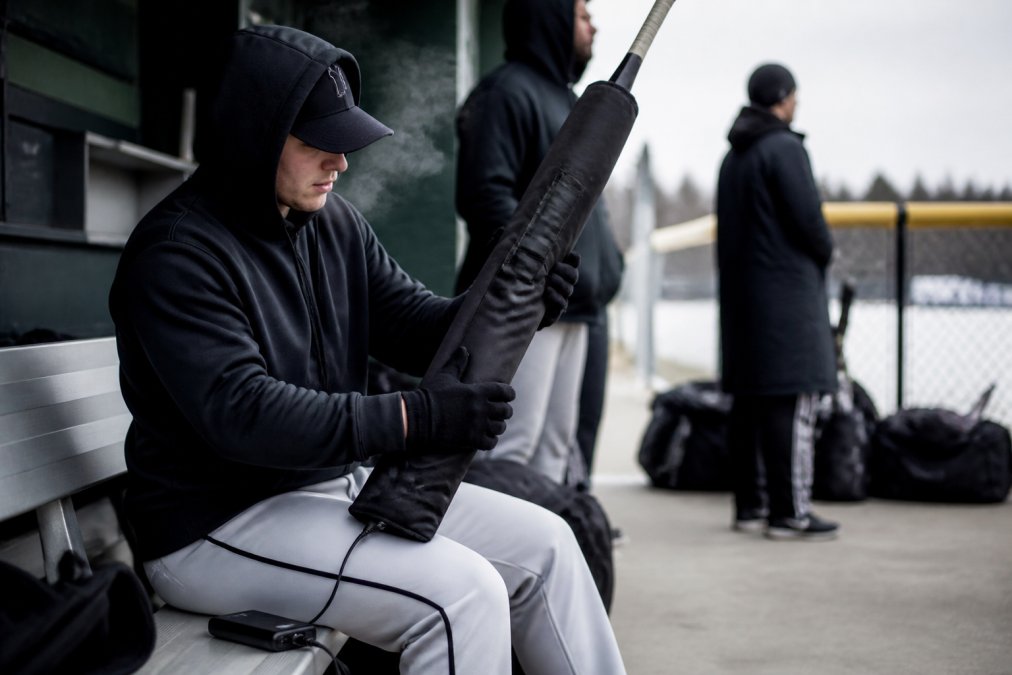 Baseball player warming a bat in a heated sleeve to see if is playing baseball in freezing weather worth it.