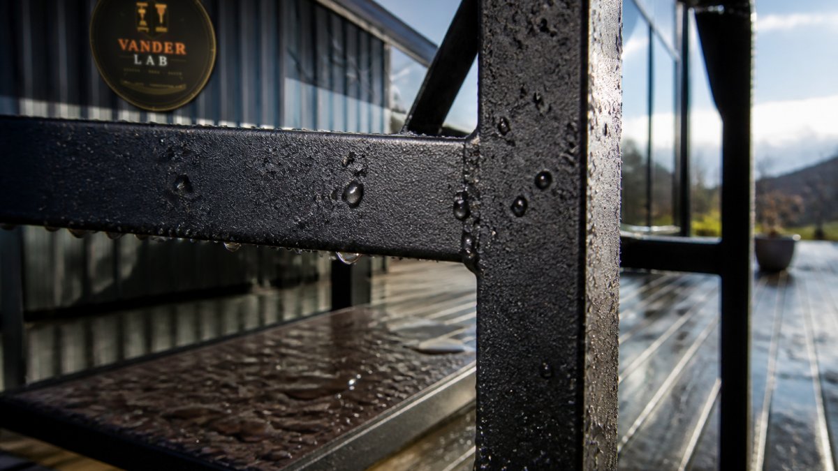 Close-up of weathered metal furniture frame showing protective powder-coated finish with visible resistance to scratches, outdoor setting with natural sunlight and rain elements