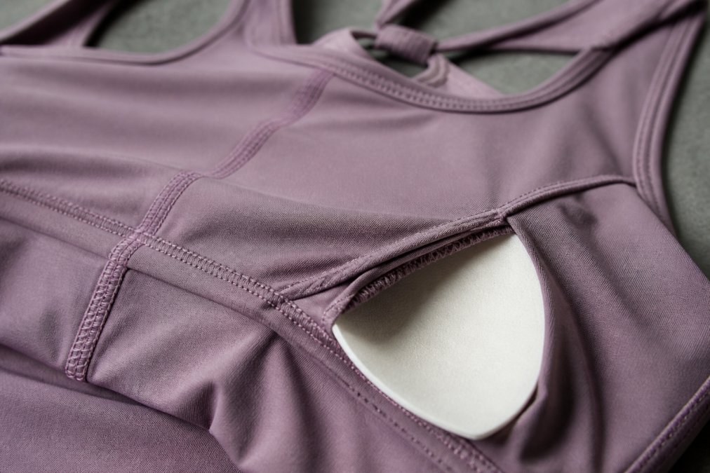 Close-up of premium activewear fabric showing flatlock seams, nylon-spandex blend texture with visible weave detail, and removable padding construction under natural studio lighting