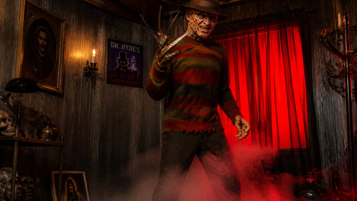 A life-size Freddy Krueger animated figure standing in a dimly lit room with eerie red lighting, clawed hand raised, surrounded by fog and vintage horror decor