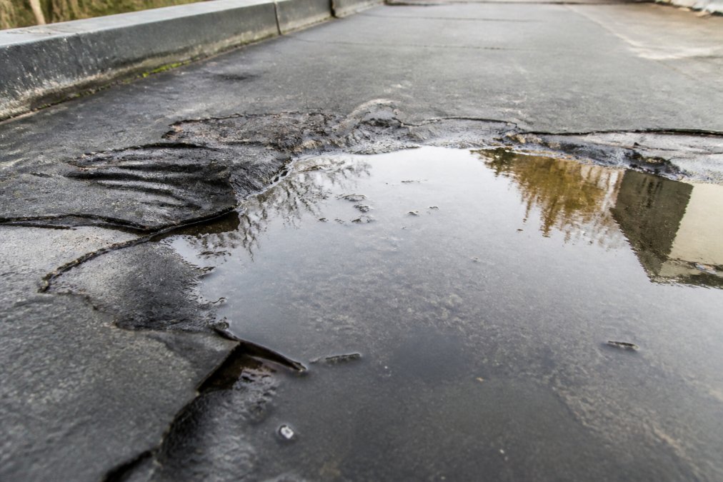 Close-up of flat roof surface showing water pooling, visible cracks, deteriorated membrane material with visible moisture damage and weathering
