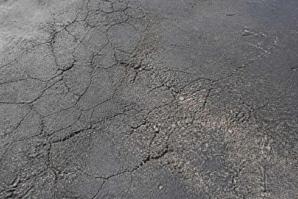 Infographic showing signs of parking lot sealcoating failure like raveling, aggregate loss, and surface cracks.