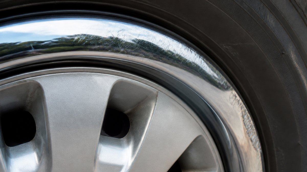 Close-up of a chrome trim ring showing visible scratches, dents, and curb damage on a vehicle wheel with natural outdoor lighting
