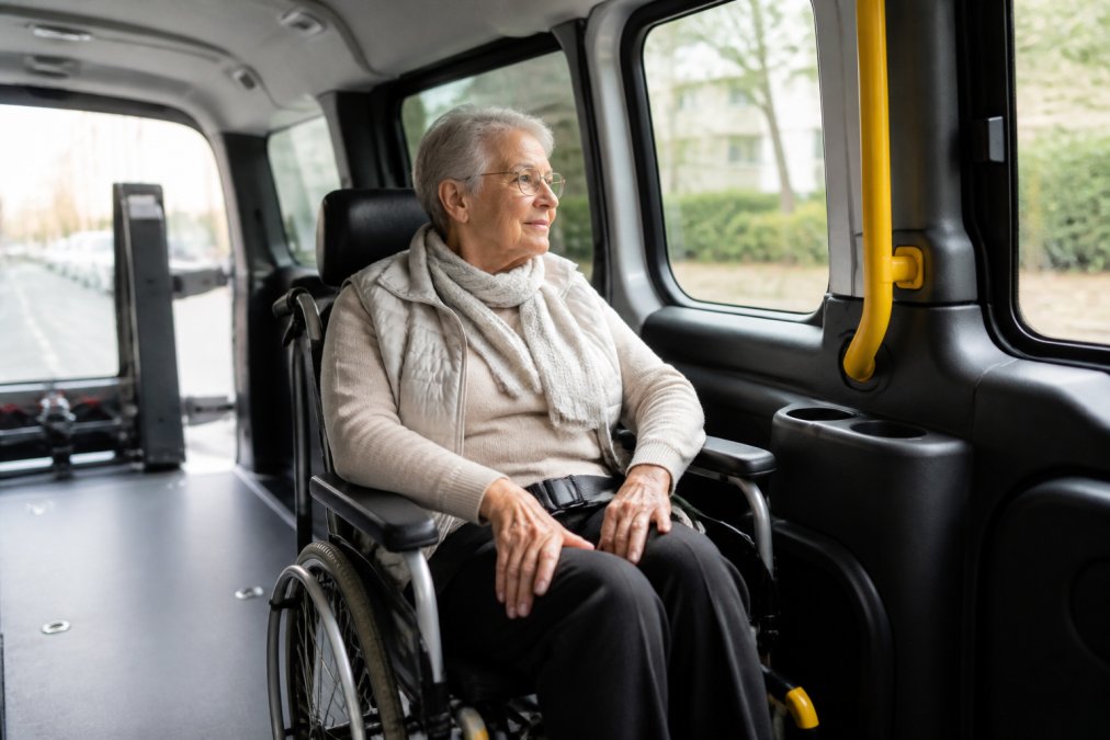 Oudere rolstoelgebruiker zit comfortabel in het interieur van een speciaal aangepast voertuig, zacht daglicht door de zijramen, ontspannen gezichtsuitdrukking, voertuiginterieur met aangepaste bekerhouders en handgrepen zichtbaar