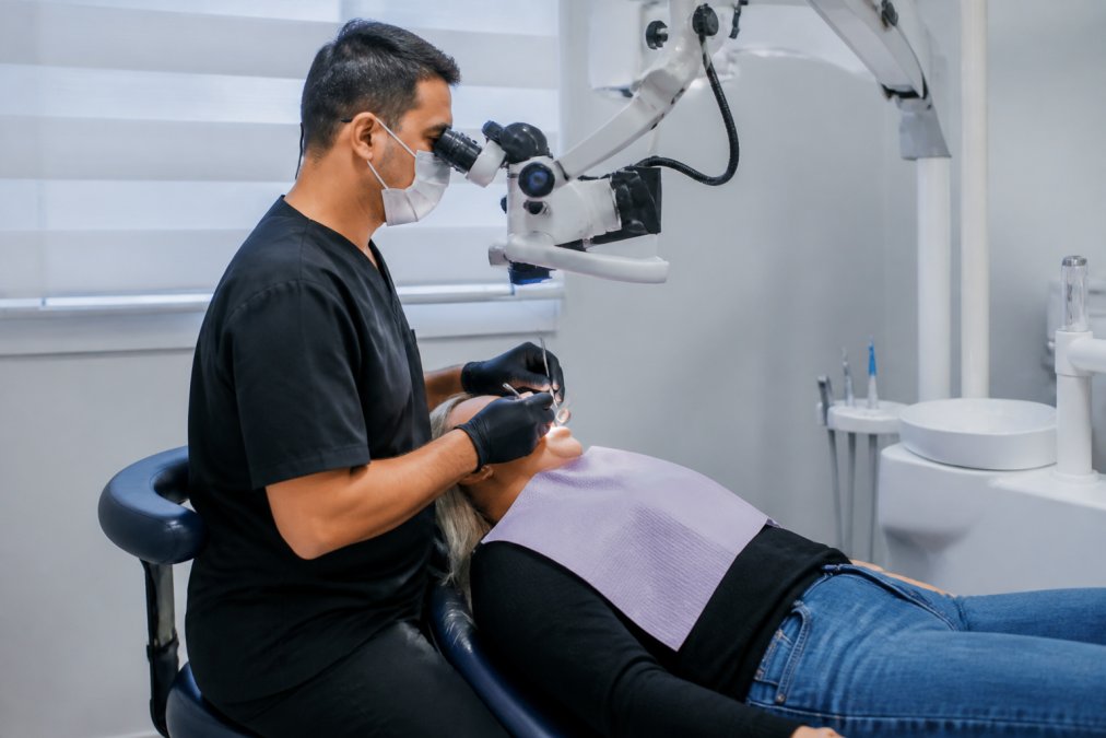 Professional dental specialist carefully performing root canal procedure with patient in comfortable dental chair, using advanced magnification and lighting in modern clinical setting