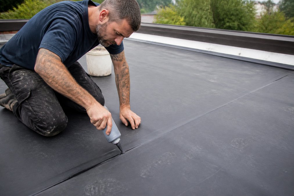 Professional roofer carefully sealing EPDM seams with specialized adhesive on a low-slope roof, showing close attention to joint alignment and proper application technique