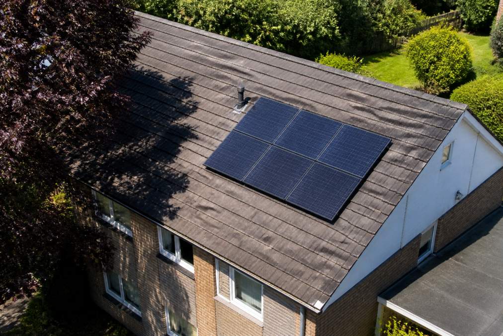 Residential property photographed from above during midday, showing a south-facing roof section clearly illuminated by direct sunlight with visible shadows from a nearby tree at the roof's edge, demonstrating the contrast between shaded and unshaded areas