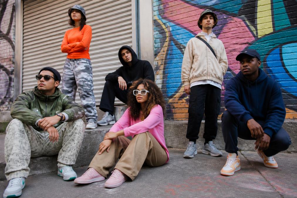 Diverse group of people wearing distinct streetwear styles in an urban setting, each expressing individual identity through color, silhouette, and aesthetic choices, shot in natural daylight with varied backgrounds showing street culture