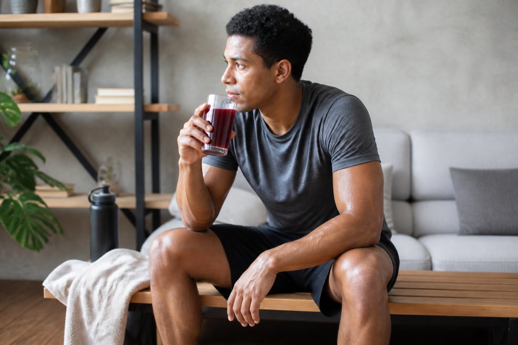 A runner sitting on a bench at home, holding a glass of dark red tart cherry juice after a workout, with a small towel nearby