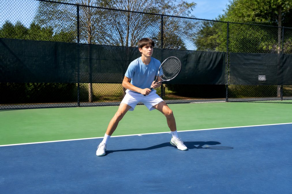 Beginner tennis player practicing split step drill on outdoor court with clear sunny conditions, demonstrating proper stance and weight distribution