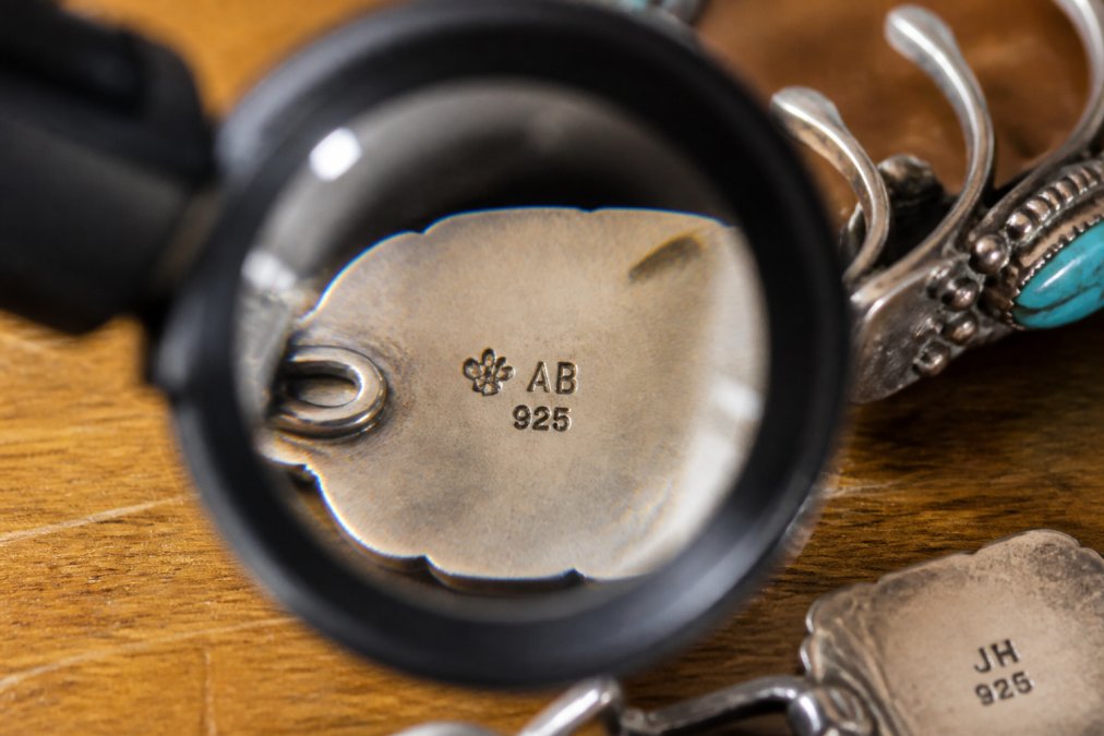 Detailed close-up of sterling silver hallmarks and maker's stamps on authentic Navajo jewelry showing crisp, hand-stamped initials, tribal symbols, and "925" sterling marking under magnification