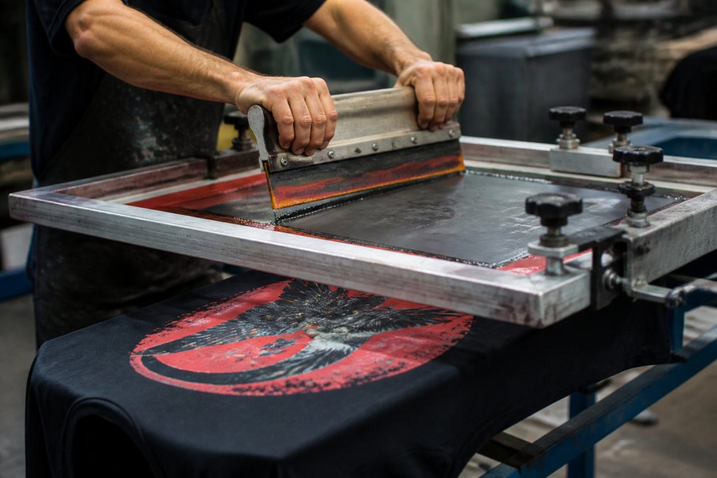 Screen printer pulling a squeegee over a vintage t-shirt design to achieve a distressed, faded look