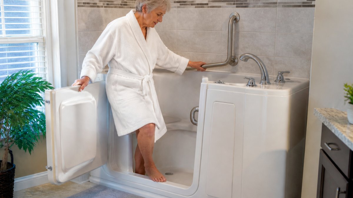 Older adult safely entering a walk-in tub with low threshold and grab bars visible, demonstrating ease of entry and secure bathing setup in a bright, modern bathroom
