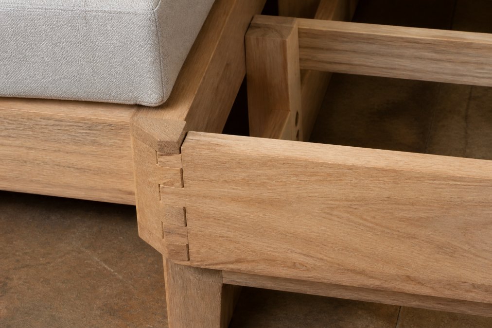 Close-up of wooden sofa frame construction showing dovetail joints and solid wood corner blocks on a modern sectional, natural studio lighting revealing grain detail and joinery technique