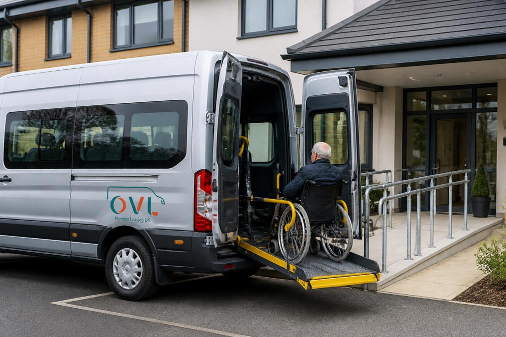 Professional wheelchair accessible minibus parked outside a modern care facility with accessible entrance ramp visible, showing the vehicle's side lift mechanism and professional branding in natural daylight
