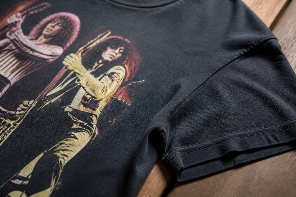 Close-up of a high-quality vintage band t-shirt showing crisp screen-printed graphic with sharp color registration, reinforced stitching at seams, and visible fabric texture with soft-hand feel