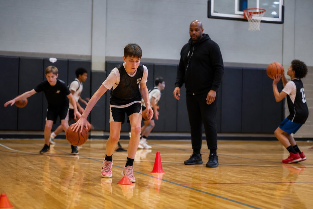Young basketball players performing dribbling drills and shooting practice during a tryout session with a coach observing and providing feedback in a gymnasium