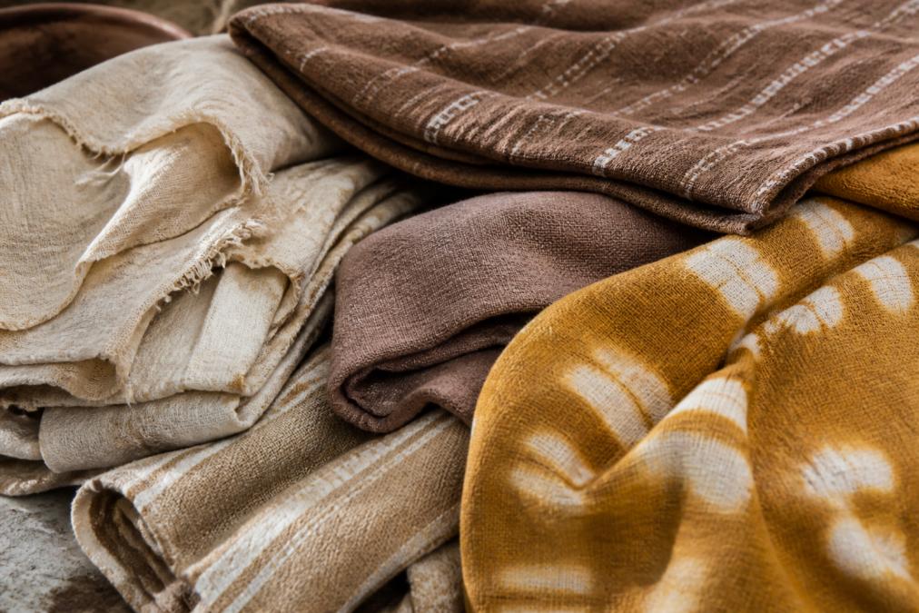 Close-up of hand-dyed natural fabric textures showing organic cotton and artisanal dye patterns in earthy tones with visible weaving detail