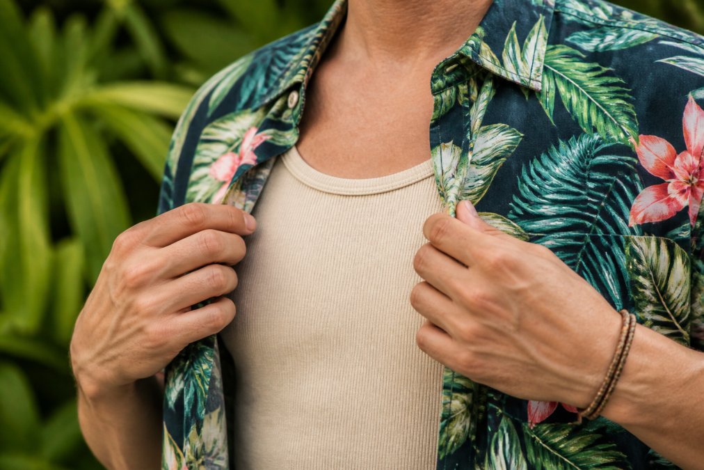 Close-up of someone layering a tropical print shirt over a neutral tank top, showing how to balance bold island prints with solid basics for everyday wear