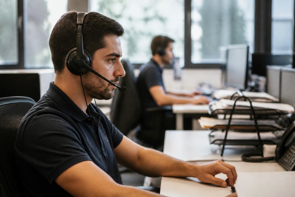 IT support professional at a modern desk with multiple monitors displaying ticket queues, alert notifications, and performance dashboards with real-time data