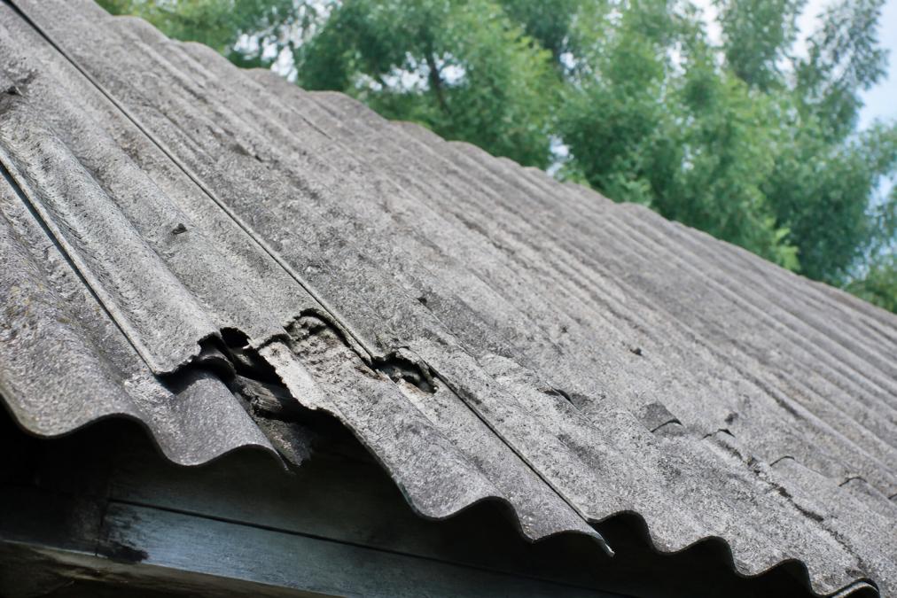 Blízký záběr na starou eternitovou střechu s viditelným šedým zbarvením, vlnitou strukturou a místy s viditelným rozpadem materiálu v přirozeném denním světle