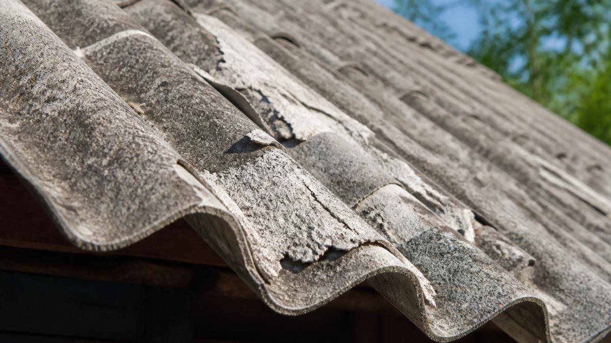 Blízký záběr na starou eternitovou střešní krytinu s viditelným poškozením, odlupováním materiálu a charakteristickou vlnitou strukturou v přirozeném denním světle
