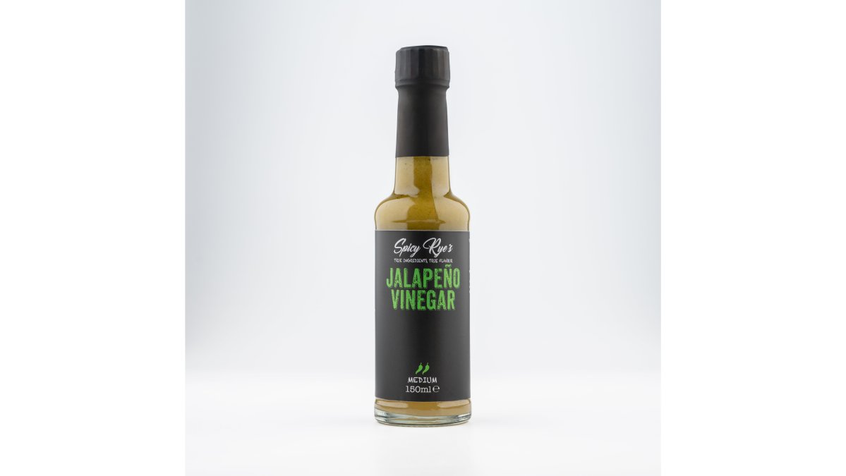 Home cook drizzling jalapeño vinegar over a fresh green salad in a bright kitchen, with vegetables and vinegar bottles visible on the wooden counter