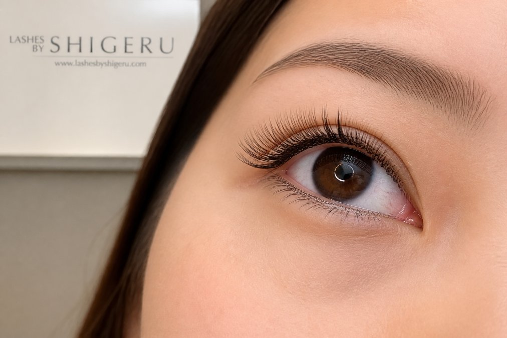 Close-up of a person's eye showing beautifully applied, feathered Japanese lash extensions with natural definition and tapered tips, photographed in professional clinic lighting