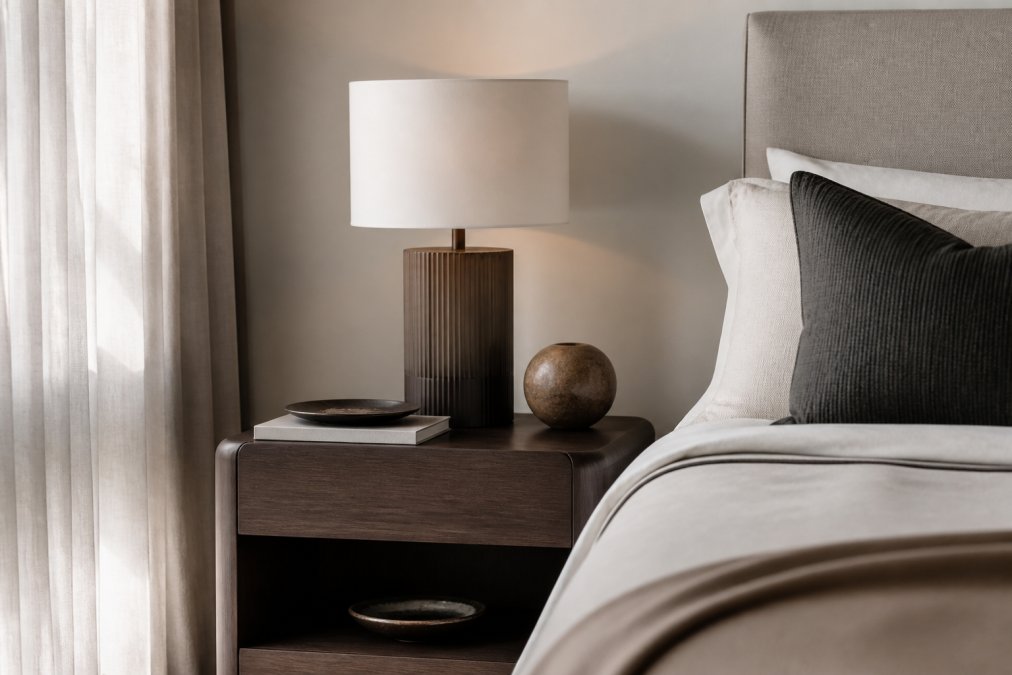 Styled bedroom interior featuring a contemporary bedside table with clean lines, soft natural lighting filtering through sheer curtains, minimalist decor with neutral tones, and carefully curated accessories reflecting modern luxury design aesthetic