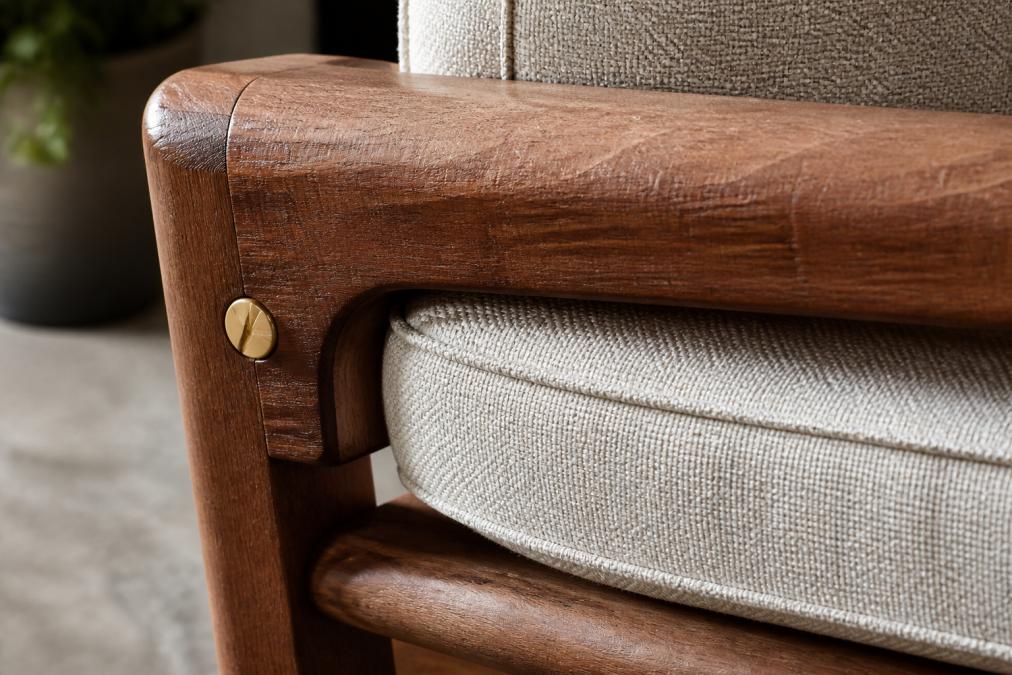 Close-up detail shot of rich timber grain texture with visible hand planing marks, brass hardware catching soft light, and layered fabric upholstery showing tight stitching and weave detail, demonstrating luxury furniture craftsmanship