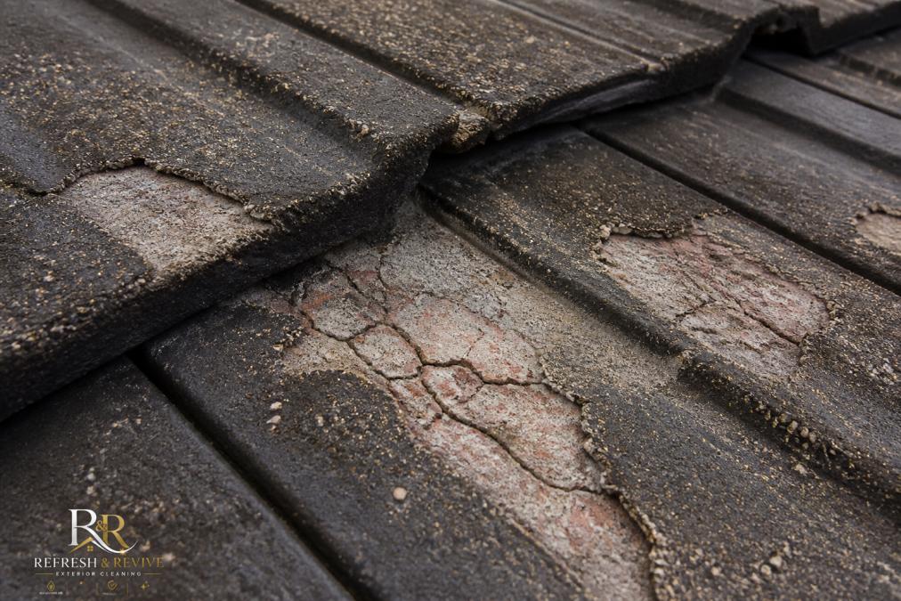 Close-up of cracked and granule-stripped roof tiles showing exposed substrate and discolouration patterns where high-pressure water has damaged protective surface layer