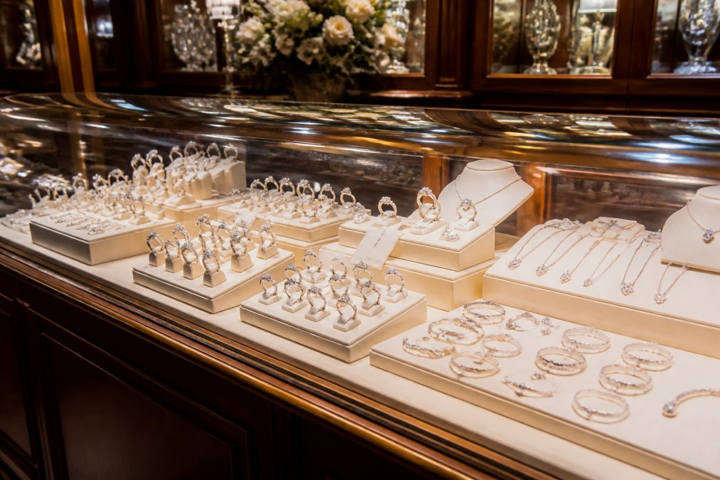 A well-presented display of diamond rings and silver jewellery arranged in a glass counter inside an elegant, traditional jeweller's shop, with warm lighting reflecting off the polished surfaces