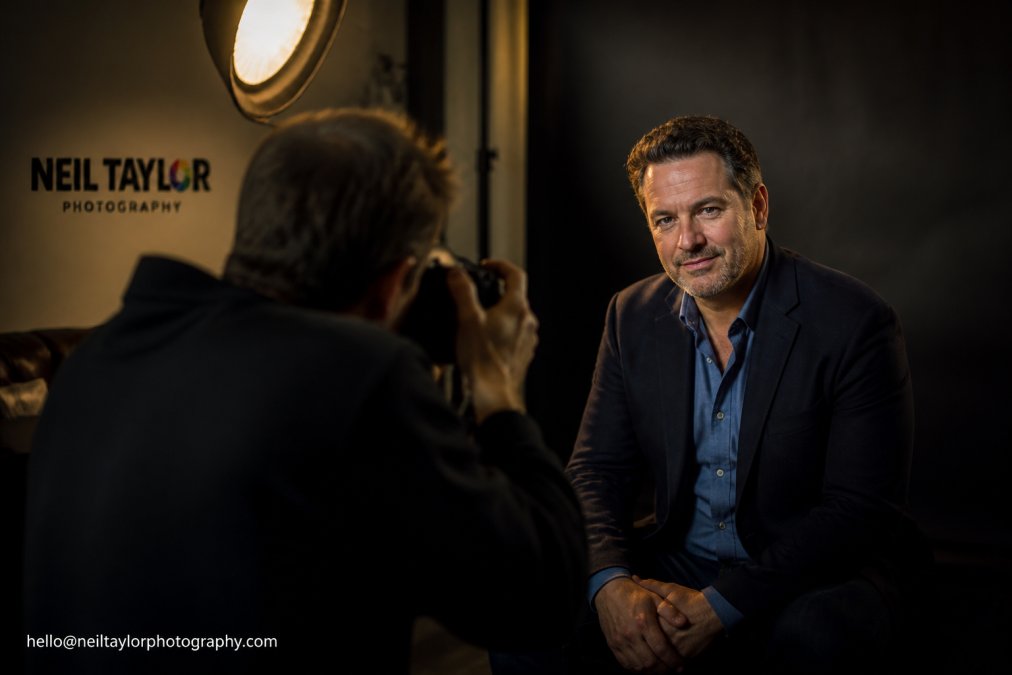 Professional actor in modern studio with soft directional lighting, wearing business casual blazer, relaxed confident posture looking directly at camera