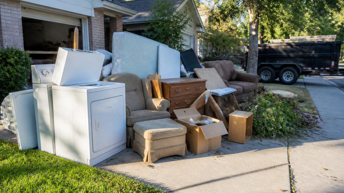 Old furniture, appliances, and yard waste piled in a driveway to estimate junk removal cost.