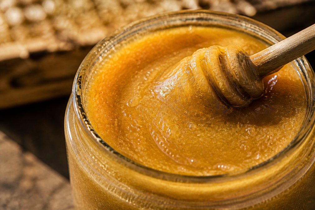 Nahaufnahme von Honig im Glas mit cremiger Konsistenz, Kristallstruktur sichtbar, natürliche Lichtbrechung zeigt die goldbraune Farbe
