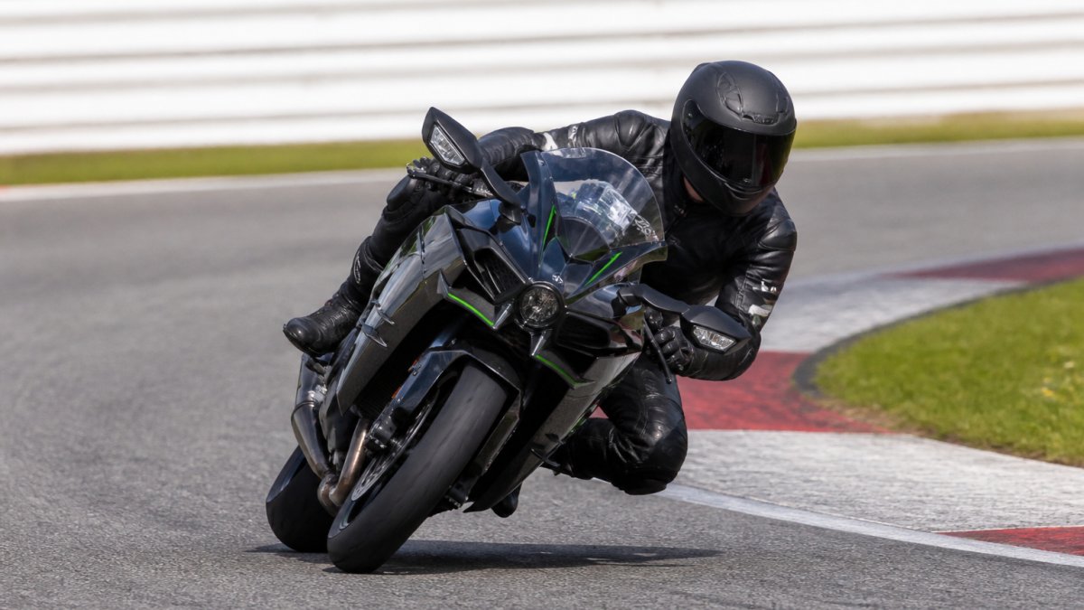 Ervaren circuitrijder op een Kawasaki H2 in een snelle bocht, lichaam ingehangen, motor gekanteld, focus op balans en voertuigbeheersing