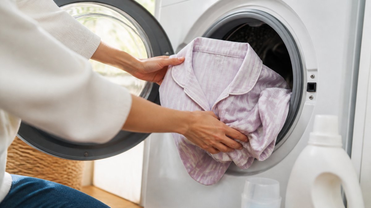 Close-up of hands placing soft cotton pajamas into a washing machine with cool water and mild detergent visible
