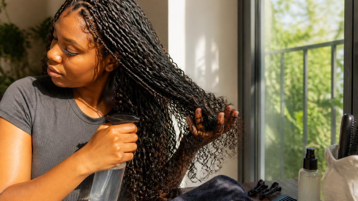 Woman refreshing goddess braids by misting curls with water spray and scrunching them upward to restore curl definition and shine in natural sunlight