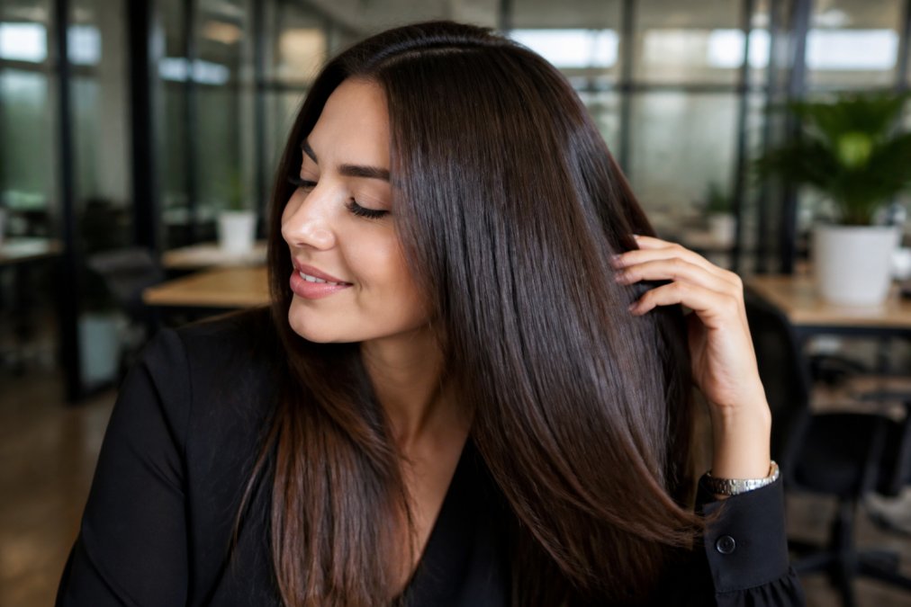 Person running fingers through smooth, shiny hair with visible shine and smoothness, demonstrating healthy keratin-treated hair texture and manageability with natural lighting