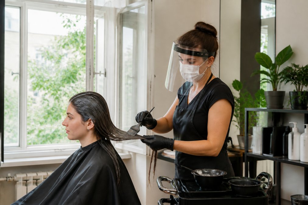 Professional stylist applying keratin treatment to client's hair in well-ventilated salon with open windows and protective equipment visible